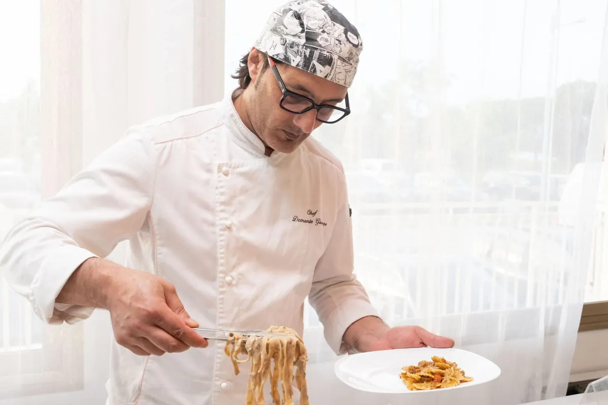 Chef plating pasta during dinner service with a dish cost sheet nearby